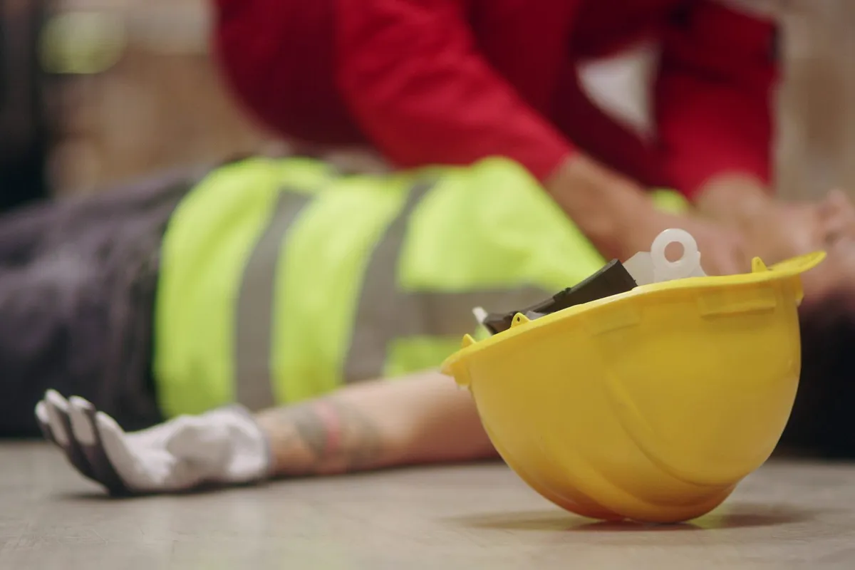 Worker in a high-visibility vest giving first aid to a colleague on a construction site